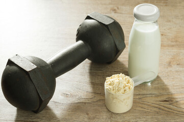 A spoon of protein powder with dumbbell and milk bottle.