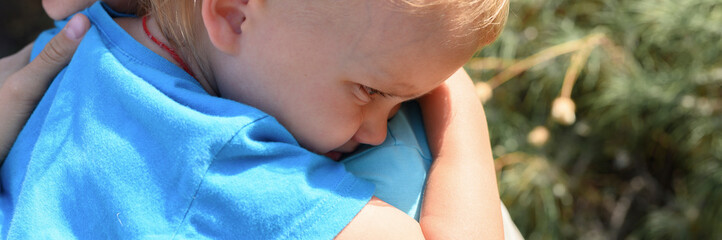 cute little upset baby boy weeping on mom's shoulder in his mother's arms, hugging his mother. banner