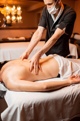 Professional masseur in facial mask doing a deep massage to a male client at Spa salon. Business during the epidemic concept