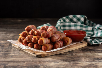 Pig in blankets. Sausages wrapped in smoked bacon on wooden table