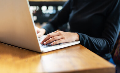 Asian woman using laptop at home while sitting the wooden table.hands typing on the notebook keyboard. Computer, laptop and studying remotely.
