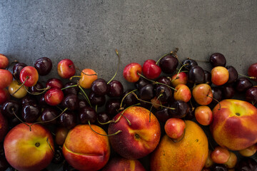 Juicy fruits and berries on a table. Dark grey textured background with copy space. Healthy eating concept. Vibrant colors of fresh fruits. 