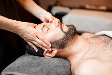 Obraz na płótnie Canvas Bearded man receiving a facial massage, relaxing at Spa salon, close-up