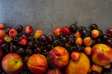 Juicy fruits and berries on a table. Dark grey textured background with copy space. Healthy eating concept. Vibrant colors of fresh fruits. 