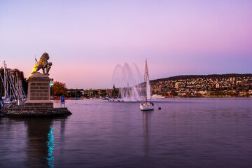 Fototapeta na wymiar Lakeside view of lake Zurich by the pier after sunset in late October with statue of lion and sailboats in the distance