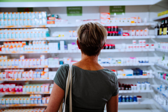 Woman walking towards shelf searching for cold and flu medication for sick husband. Searching in drugstore pharmacy