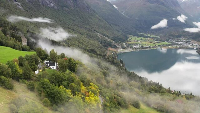 Loen Village on Scenic Coast of Innvikfjorden, Norway. Aerial View of Summer Fog Above Green Hills and Fjord Water, Drone Shot