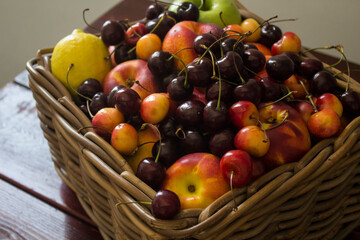 Summer fruits in basket on wooden table. Vibrant colors of beautiful cherries, apples  and nectarines. Healthy eating concept. Fresh fruits close up photo. 