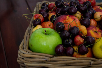 Summer fruits in basket on wooden table. Vibrant colors of beautiful cherries, apples  and nectarines. Healthy eating concept. Fresh fruits close up photo. 