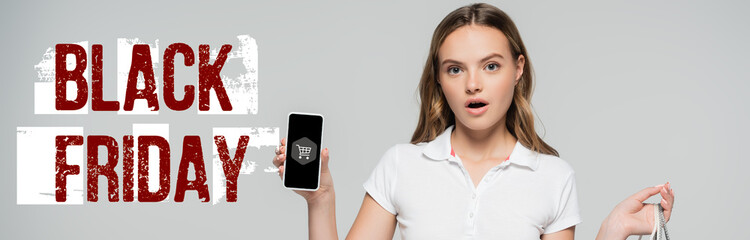 Fototapeta premium shocked woman holding smartphone near black friday lettering and cart illustration on grey, banner