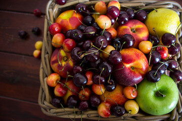 Summer fruits in basket on wooden table. Vibrant colors of beautiful cherries, apples  and nectarines. Healthy eating concept. Fresh fruits close up photo. 