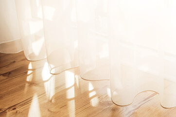 Transparent white curtain tulle from an open window. Sunny day, the sun's rays sunlight penetrate...