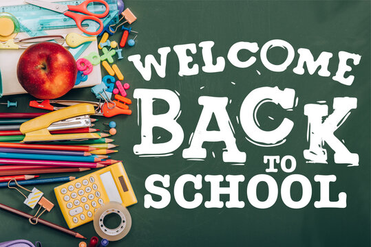 top view of ripe apple, calculator and school stationery on green chalkboard with welcome back to school lettering