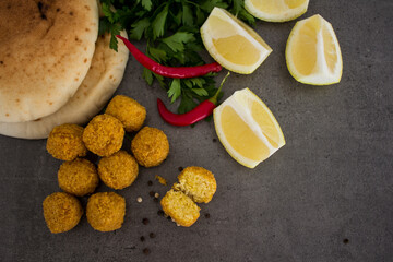 Fresh made falafels on dark grey table with lemon slices, chili pepper and parsley. Authentic food of Israel. Ingredients top view photo. Healthy eating concept. 
