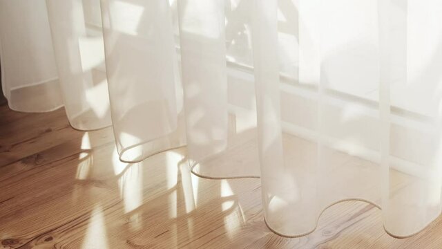Transparent white curtain tulle moves from the wind from an open window. Sunny day, the sun's rays sunlight penetrate the room.