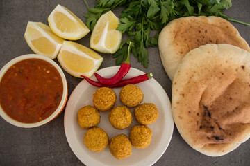 Falafel - authentic food of Israel. Fresh ingredients top view: plate of falafels, pita bread, parsley, harissa sauce, lemon, parsley and red pepper.  Dark grey background with copy space. 