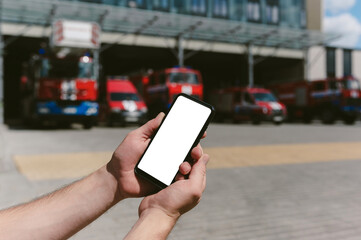 Mock up of a smartphone in the hands of a man. Against the background of fire trucks and the station.