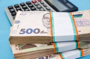 bundles of hryvnia and a calculator on a blue background. A stack with 500 hryvnia. Much money.