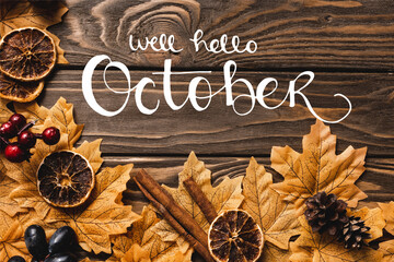 Top view of autumnal decoration and foliage near well hello October lettering on wooden background