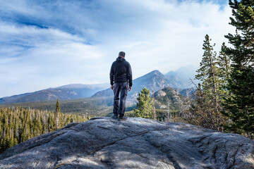 Man standing on a summitin the Rocky Mountain National Park and watching the smoke from the wildfires coming in the valley