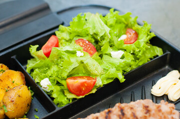 Restaurant lunch, content for the site about food and pages in social networks. Breakfast, cutlet or steak, tomato salad, fried potatoes, croutons and fried egg on black plate.