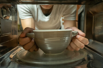 Men's gray hands get a bowl out of the microwave is a close-up photo from the inside.