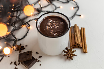 Hot chocolate , winter drink in a white mug with cinnamon, star anise, chocolate on a white plate with a Christmas garland.