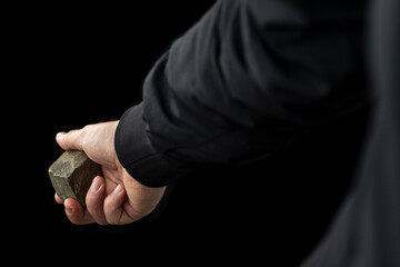 Cobblestone in male hand on black background. Riot concept.