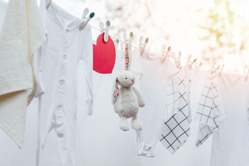 White washed baby clothes, toy and red heart on clothesline with plastic pins.