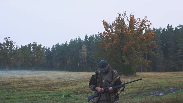 A hunter with a gun tracks down the prey. Aim a hunting rifle. Beautiful autumn forest.