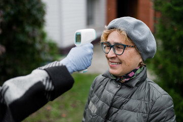 A doctor measures the temperature of an elderly woman wearing a mask with a non-contact infrared...