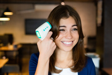 Caucasian woman holding an infrared thermometer to her temple like a pistol. Checking the...