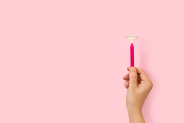 Mano femenina sosteniendo una maquinilla de afeitar sobre un fondo rosa pastel liso y aislado. Vista de frente y de cerca. Copy space - obrazy, fototapety, plakaty