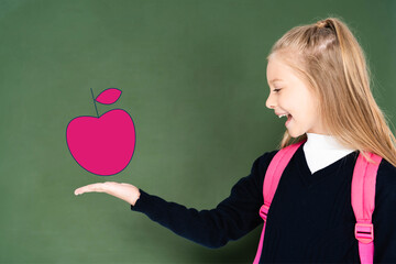 schoolgirl pointing with hand at illustrated pink apple on green chalkboard