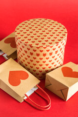 Valentine's Day concept. Shopping paper bags and round gift box with hearts print on red background. 