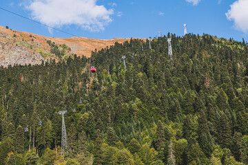 Aerial lift cabins in mountain. Cable car at ski resort. Ski lift red cabins and forest in background. Vacation and ecotourism in Caucasus mountain.