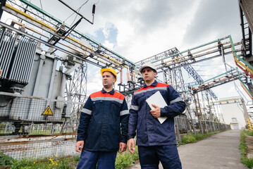 Two specialist electrical substation engineers inspect modern high-voltage equipment. Energy....