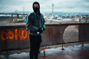 Young protester hide his identity and looks around while makes corona graffiti