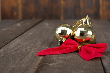 Golden christmas balls and red gift bow over wooden table with copy space