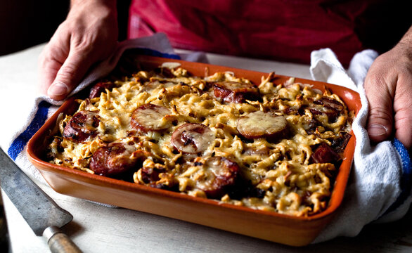 Close up of man holding spaetzle with smoked kielbasa and caramelized onions