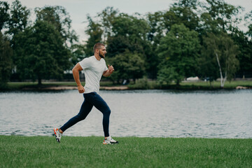 Full length shot of fast male runner runs along river, enjoys speed, photographed in motion,...