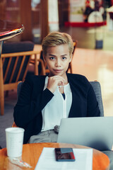 Serious business woman sitting in cafe working on laptop and looking in camera