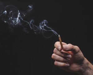 Burning tibetan incense stick in hand on dark surface