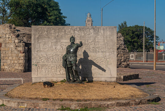 Montevideo, Uruguay- December 18, 2008: Statue of Hernandarias, Hernando Arias de Saavedra, bronze agaisnt cement wall with edged images under blue sky with green foliage.