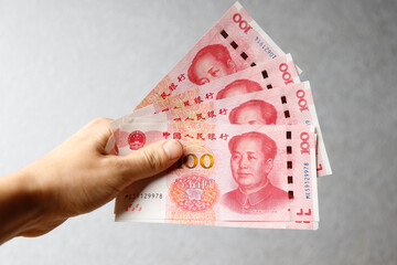 Hand holding one hundred Yuan notes against gray background