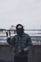 Anonymous in mask and glasses checks spray paint can on the roof