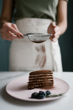 Woman pouring cocoa on chocolate cake