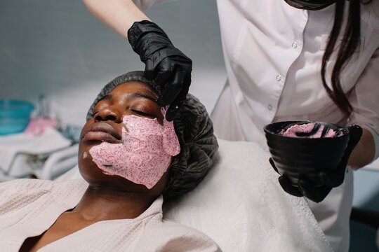 Cosmetician apply pink alginate mask on client;s face