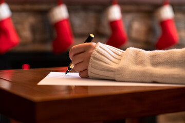 Hand of young woman with fountain pen and sheet of paper on background of christmas tree and...