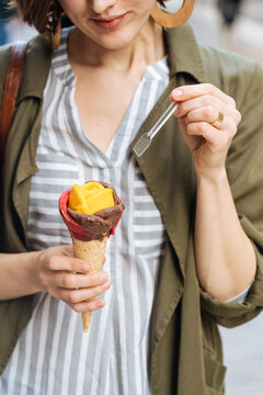 Delighted woman trying exotic ice-cream with spoon on street